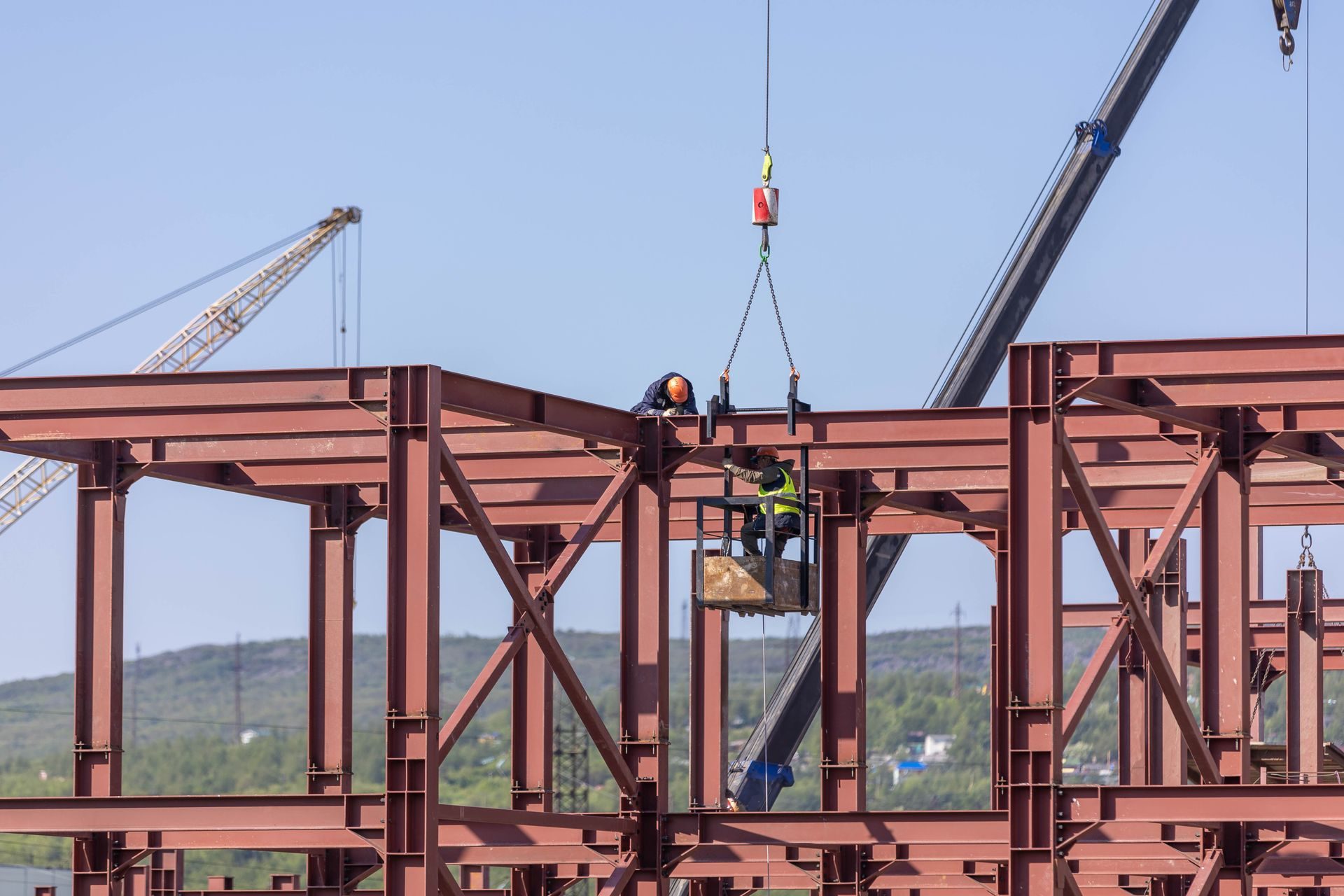 Ironworkers erecting a red structural steel frame with a crane