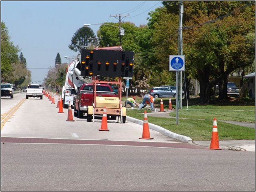 Crew pouring concrete at a roadside bus stop behind traffic cones