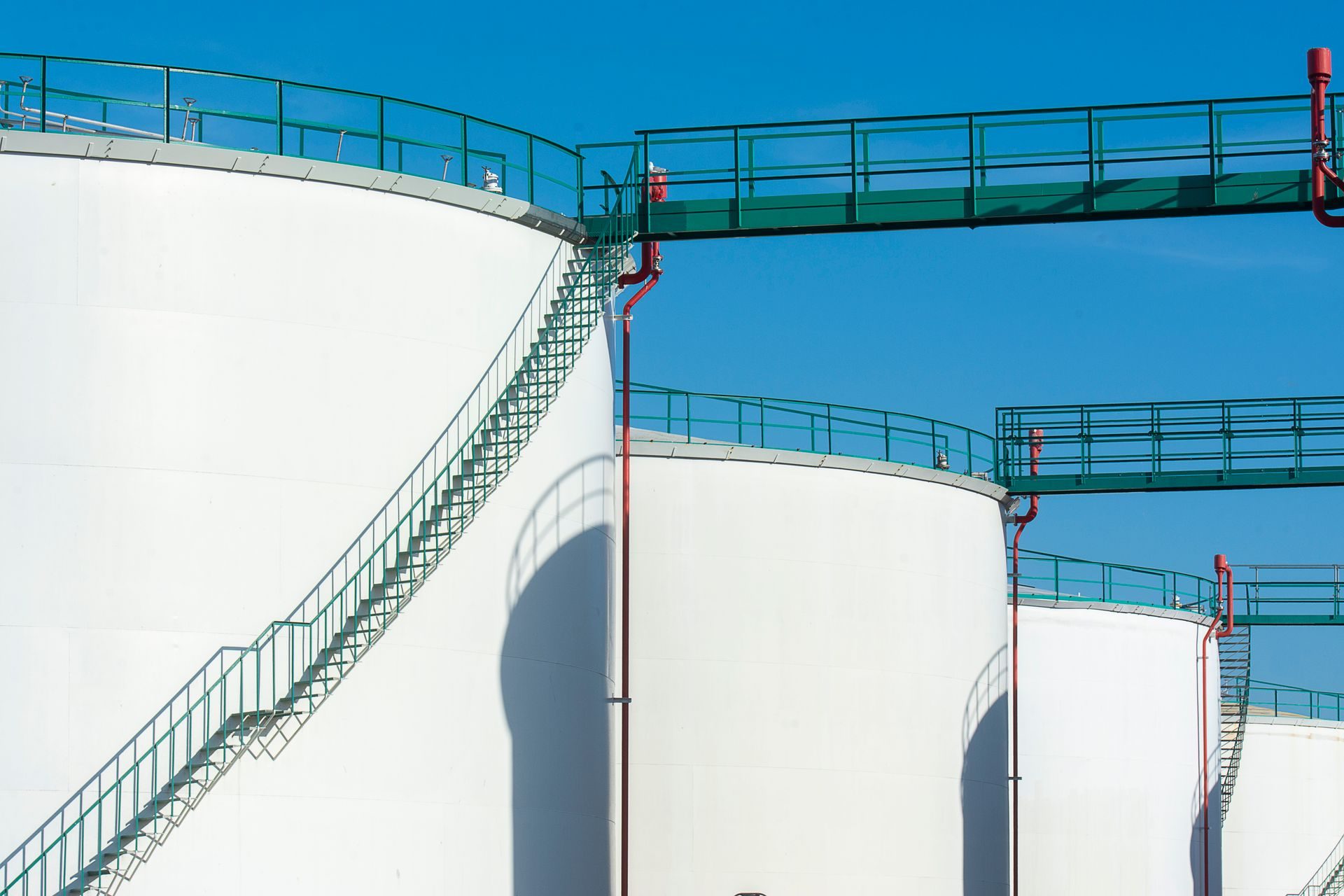 White above-ground fuel storage tanks linked by green catwalks under a blue sky