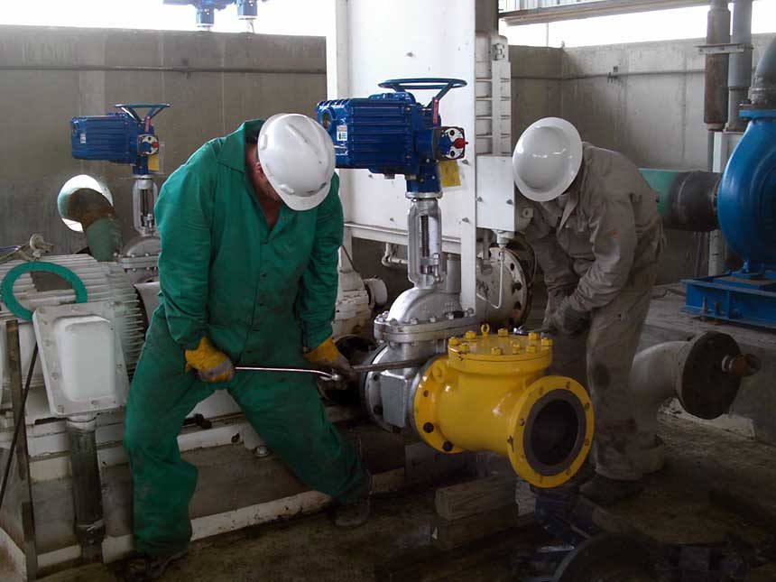 Two workers in hard hats servicing a yellow valve on an industrial pump line